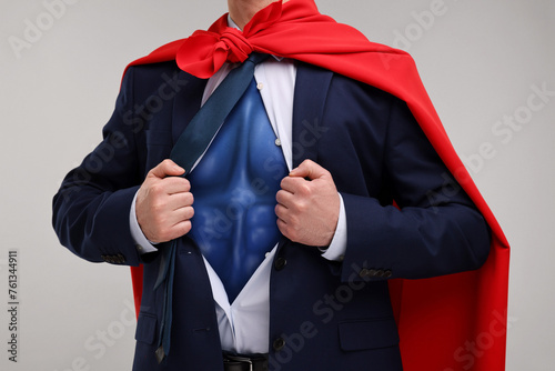 Businessman wearing superhero costume under suit on light grey background, closeup