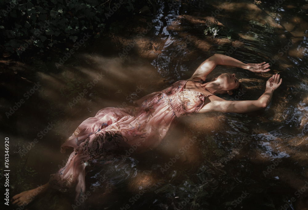 The stretched body of a woman floats on the healing water of the river. Concept of spiritual connection with the natural environment and ethereal atmosphere between two worlds. - obrazy, fototapety, plakaty 