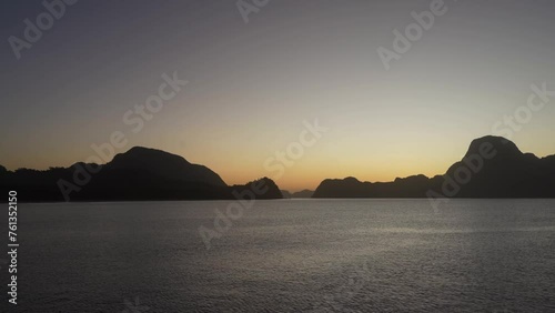 Twilight after sunset on a tropical island. The surface of the ocean undulates calmly. Ripples on the water. Picturesque mountains against the evening sky, highlighted in orange. Philippines. Palawan.