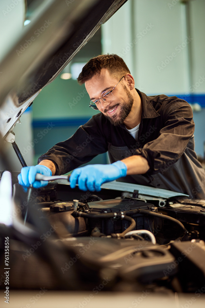 A smiling mechanic is using some tools at his car repair service, working. A smiling mechanic is using some tools at his car repair service, working.