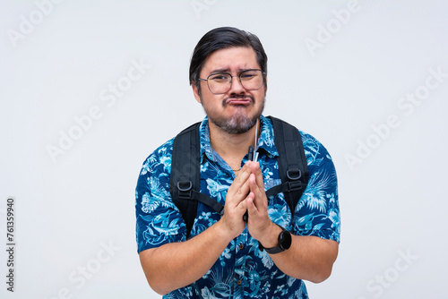 Canvas Print A middle-aged male tourist with clasped hands and a pleading look, wearing a blue floral shirt, isolated on a white background