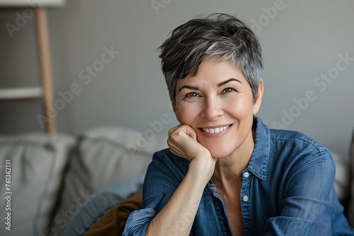 Happy attractive middle aged retired woman looking at camera, holding video call conversation with friends or family, sitting on cozy sofa at home. Relaxed mature grandmother enjoying peaceful moment.