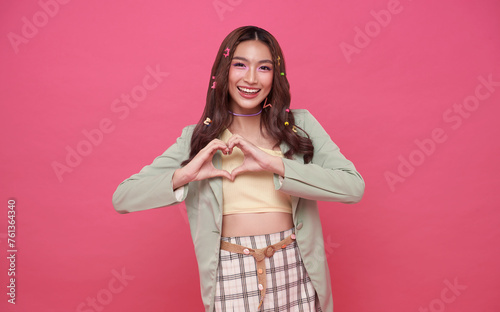 Smiling young asian girl showing heart with two hands, love sign. Isolated on pink background.