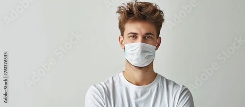 A man wearing a face mask is standing with crossed arms, sporting facial hair and wearing a Tshirt with sleeves. He may also be equipped with eyewear or sports gear for added protection photo