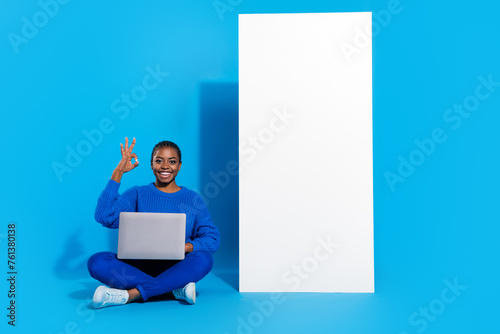 Portrait of attractive trendy cheery girl sitting using laptop showing ok-sign copy space isolated over bright blue color background