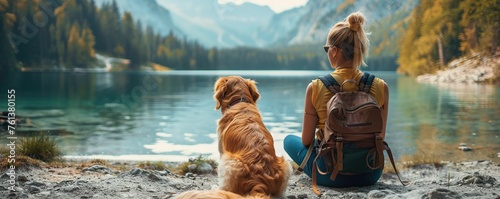 back view of unrecognizable female tourist sitting on the floor looking at the lake with cute calm dog
