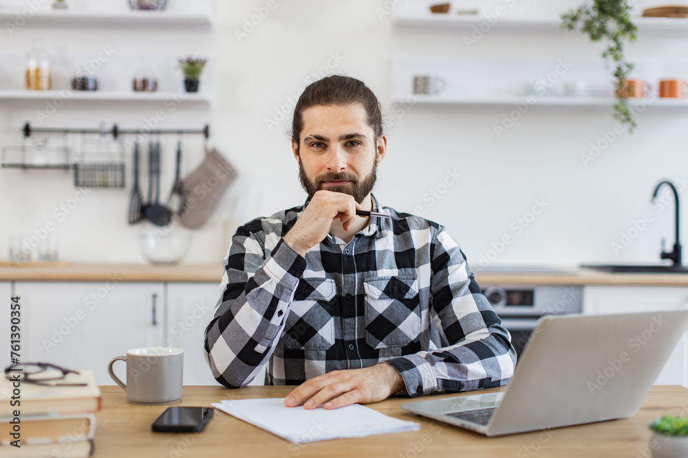 Portrait of smiling business person wearing casual clothes posing with pen, documents and portable computer. Cheerful Caucasian consultant offering guidance to clients over digital platform from home.