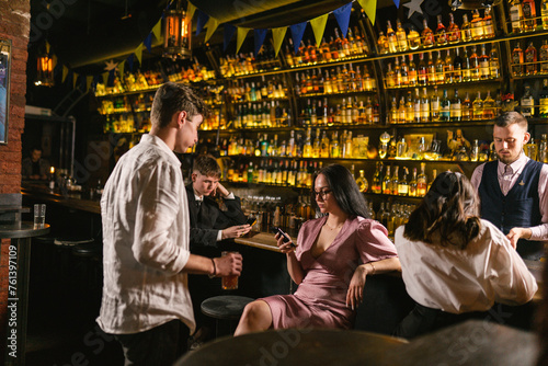 Stylish guy wants attention from busy girl sitting with phone at bright bar. Relax with delicious beverages in Ukrainian pub