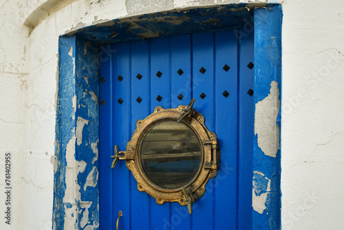 Close-up of the blue door of a white lighthouse with a peephole made from the porthole of a boat, Italy
