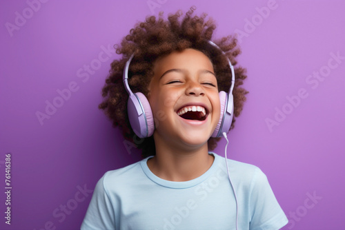 A cheerful kid model, enjoying music on headphones against a lavender solid wall background.