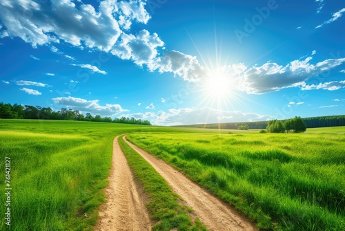 landscape with road and field. A rural road through a green meadow, blue sky and shining sun. Background. © BetterPhoto