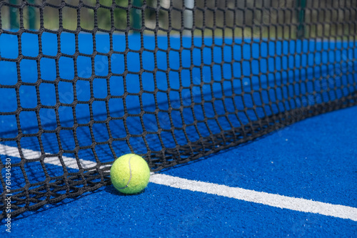A paddle tennis ball is sitting on a blue court with a net, racket sport