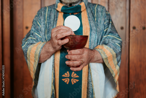 Anonymous priest elevates the Eucharistic host above a chalice, a central ritual in the celebration of the Christian Communion service photo