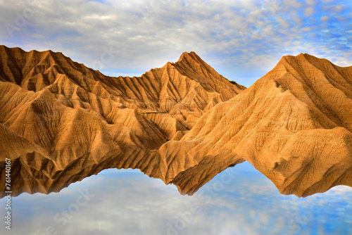 Perfect reflection of the detailed ridges of badlands in still water, creating a symmetrical visual illusion of this rugged landscape under a cloud-speckled sky photo