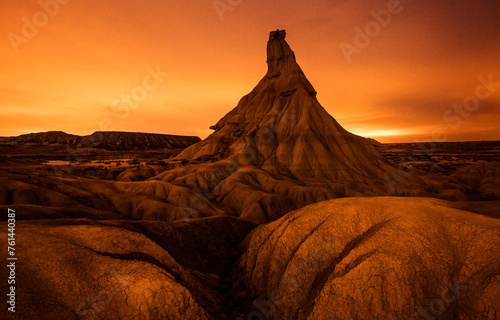 An awe-inspiring badlands spire stands tall under a fiery sunset sky, with intricate erosion patterns sprawling across the foreground photo