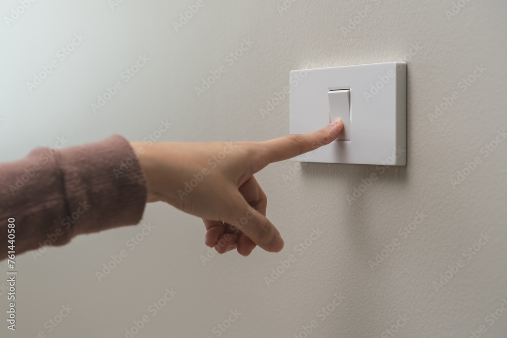 Close up of hand of woman turn off on lighting switch at home room. Finger pushing light switch turn on or off white switch on wall for saving, control power electrical energy, eco environment concept - obrazy, fototapety, plakaty 