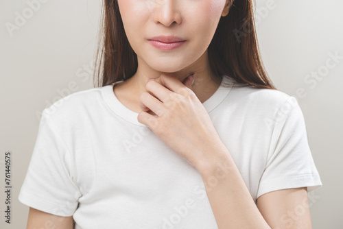 Photos Sickness in inflaming asian young woman, girl use hand check self touch at sore throat, pain thyroid gland on neck or disease reflux, acid of suffer people on wall background