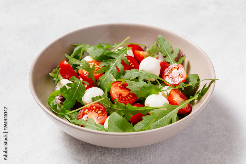 Fresh green salad made with mozzarella cheese, cherry tomatoes, arugula and olive oil on white stone table background. Healthy food and diet concept. Fresh green salad made with mozzarella cheese, cherry tomatoes, arugula and olive oil on white stone table background. Healthy food and diet concept.