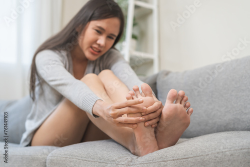 Foot pain concept, close up hand of young woman rubbing, massaging sore feet area of pain, girl suffering on sofa, couch at home. Discomfort painful feet ache from walking for long. Physical injury. photo