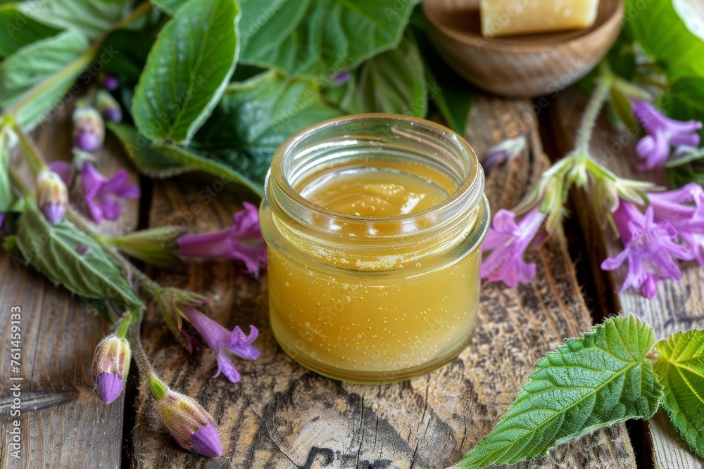A jar of homemade Comfrey (Symphytum officinale) ointment, surrounded by fresh Comfrey leaves and flowers on a rustic wooden table. Homemade remedy, natural ingredient, therapeutic atmosphere, natural