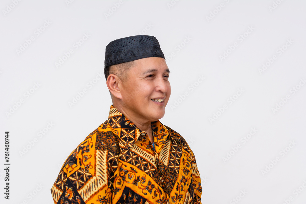 A cheerful Indonesian man wearing a patterned batik shirt and a songkok, representing traditional culture and attire.