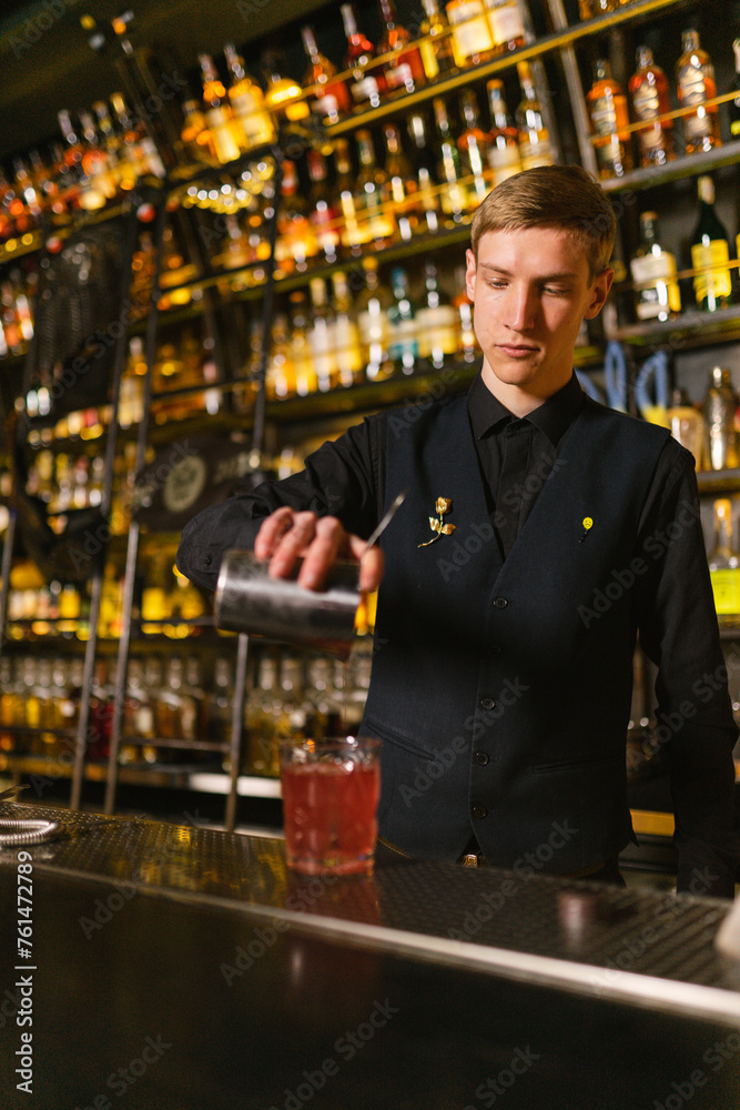 Skilled barman makes refreshing cocktail using elite alcohol. Bartender with metal bar pitcher stands by counter ready to take orders from bar guests