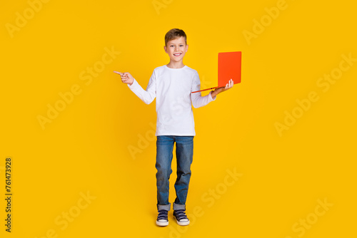 Full length photo of positive cheerful boy wear white shirt texting modern gadget showing empty space isolated yellow color background
