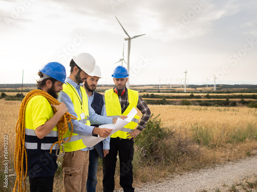 Group of male technical workers and engineers watching a blueprint in a windmill field