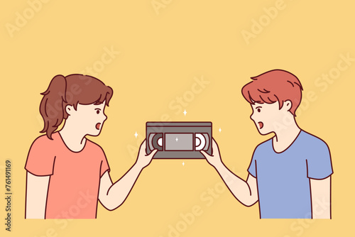 Surprised children are looking at film video cassette with movie recorded for VHS player from last century. Little kids see VHS tape for first time to play video on TV and dont know how to run cinema