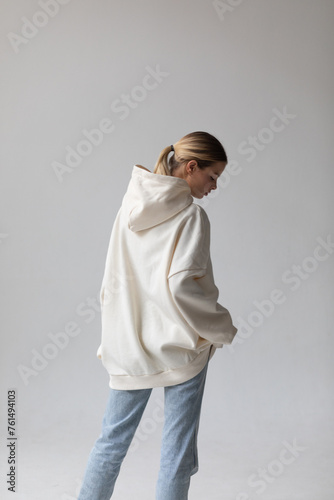 Fotografía Beautiful blonde woman in a white hoodie and blue jeans posing on a white backgr