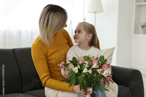 Little daughter congratulating her mom with Mother`s Day at home. Woman holding bouquet of alstroemeria flowers photo