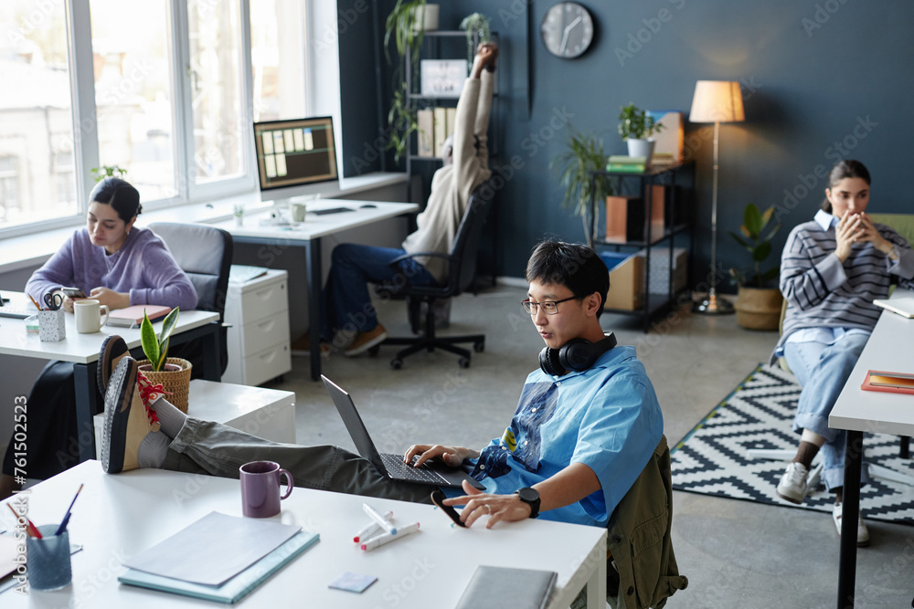 High angle view of diverse young people working in open office space with focus on creative Asian man at desk in foreground High angle view of diverse young people working in open office space with focus on creative Asian man at desk in foreground