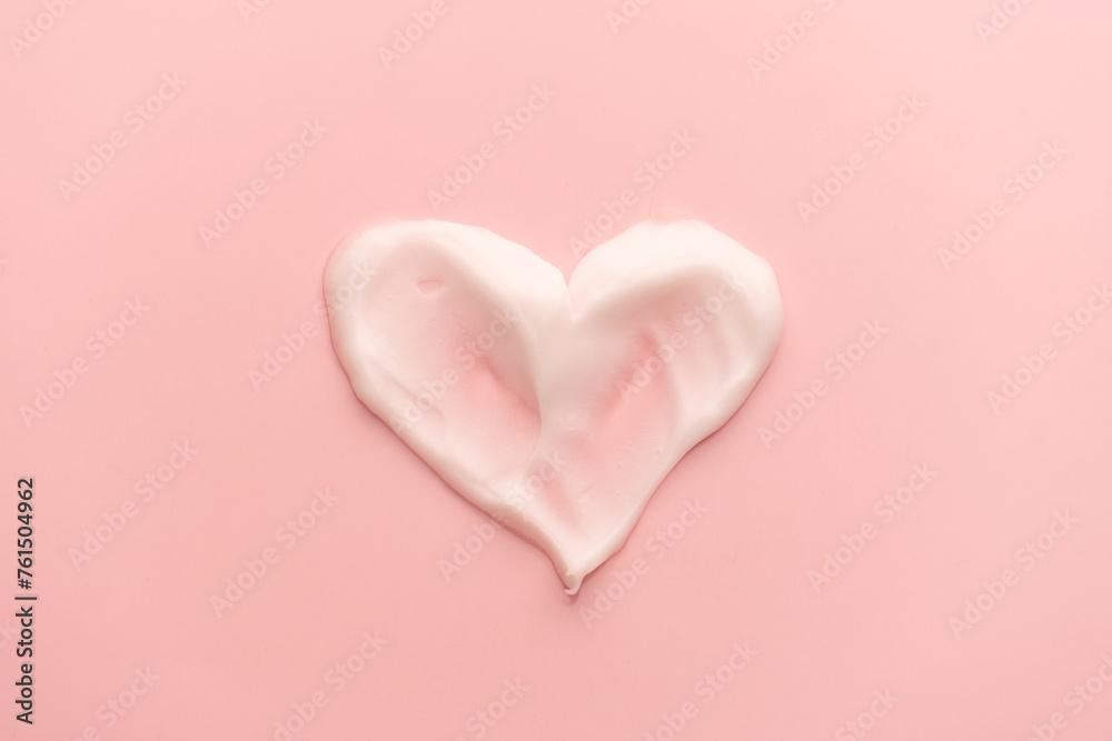 Heart shape skincare cream smear on pink background. Cosmetic lotion swatch texture of face cream, body moisturiser and hair conditioner. Beauty and cosmetic product.