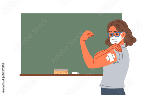 Vaccinated female teacher demonstrates patch at injection site on arm, standing near school board. Vaccinated girl teacher recommends taking preventive measures to protect against virus