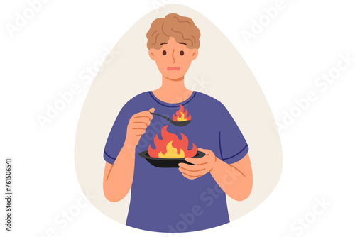 Man eats very spicy food, causing burning sensation in mouth due to overabundance of pepper, holding plate and spoon with flame. Guy eats spicy dish with spices, makes dissatisfied grimace