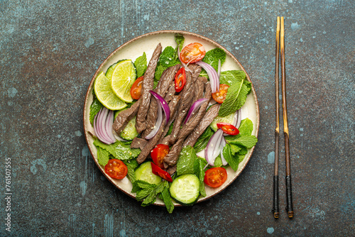 Plate with traditional Thai beef salad with vegetables and mint top view served on rustic concrete stone background, healthy exotic asian meal.