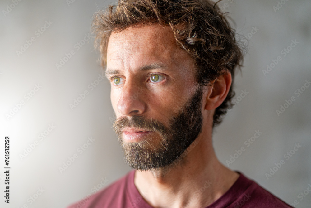 Portrait of a attractive handsome young man with beard looking outside of the window. Confident and serious look close-up photo.  - obrazy, fototapety, plakaty 