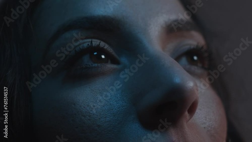 Close up on eyes looking up to a screen colours change on woman's face