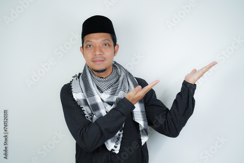 Cheerful handsome Asian Muslim man wearing Arab turban sorban pointing hand finger at empty space for advertising on isolated background photo