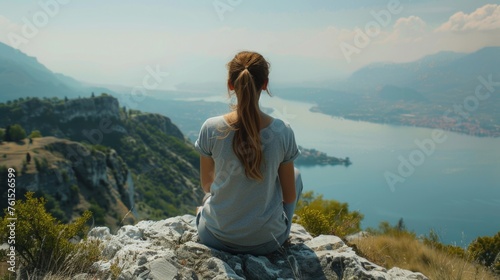 A woman sitting on a rock overlooking a serene lake. Suitable for nature and relaxation concepts #761526599
