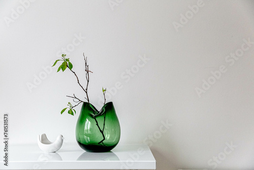 Tree branch or plant growing in a glass green vase. Hygge concept. Bird ceramic vase and candle flower. Spring stylish decoration. Easter. Mimimalism. White wall background. Eco home. photo