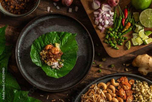 Miang Kham. Thai herbal appetizer wrapping ingredients consist of dried shrimp, roasted coconut, beans, ginger, lime, chili, and herbs into fresh Betel leaves on a wood background. photo
