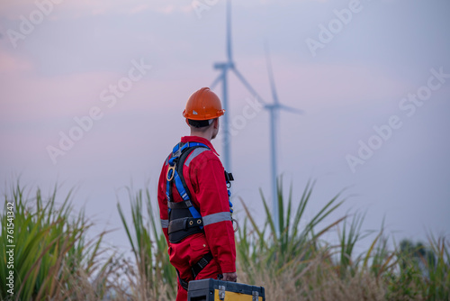 Engineer wearing uniform hold equipment box inspection work in wind turbine farms rotation to generate electricity energy. Green ecological power energy generation wind sustainable energy concept. 