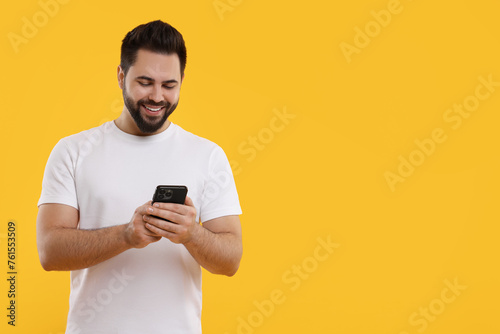Happy young man using smartphone on yellow background, space for text © New Africa