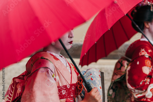 Two maiko geisha carries her red parasol with poise, her floral kimono a testament to the timeless beauty of Japanese cultural dress. photo