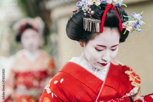 A geisha in a vibrant red kimono contemplates quietly, her face a study of elegance. Her elaborate hair ornaments signal her status in Japanese cultural tradition photo