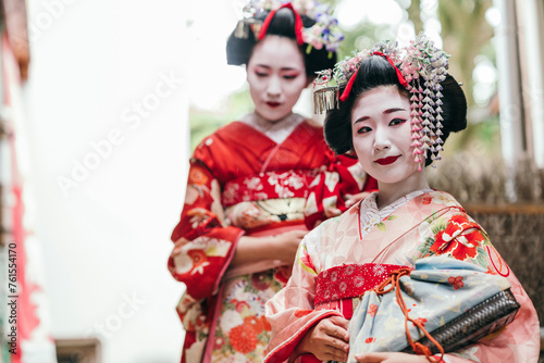 A pair of geishas in exquisite kimonos pause thoughtfully, their expressions a blend of tradition and the fleeting nature of the moment. They epitomize the timeless allure of Japanese culture photo