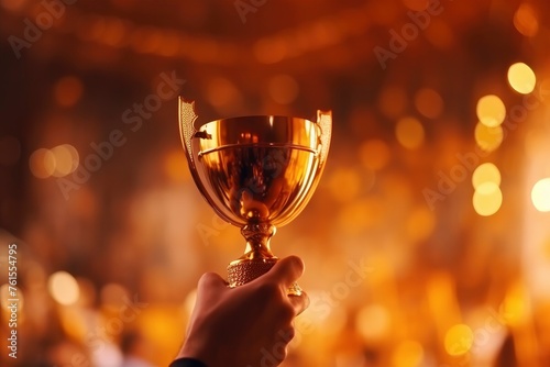 A man's hand holds gold trophy, sports cup on beautiful gold background with bokeh sparkles. Concept of victory, success, achieving a goal in sports or work, business. Place for text