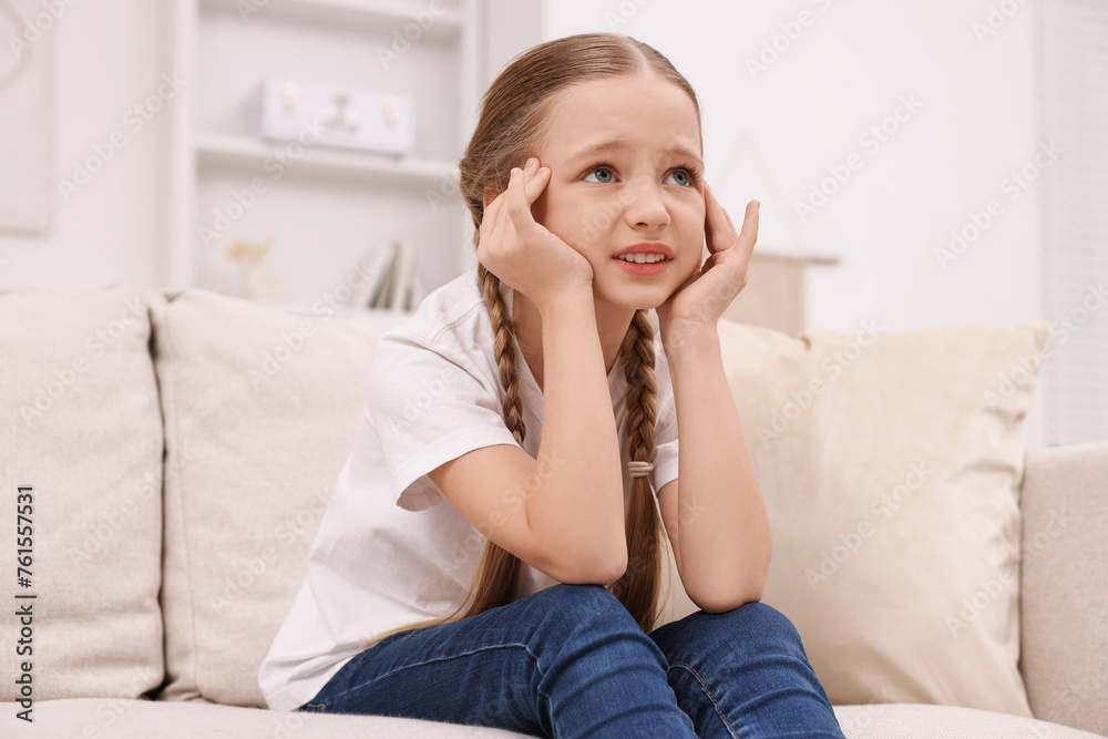 Little girl suffering from headache on sofa indoors Little girl suffering from headache on sofa indoors