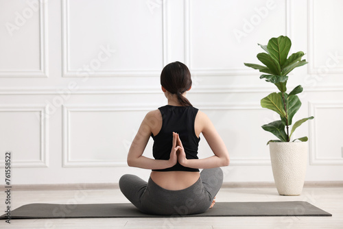 Girl practicing vajrasana with namaste behind back on mat in yoga studio